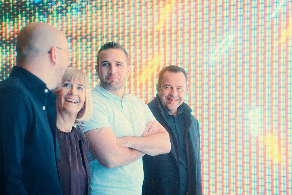 four people laughing infront of a LED screen