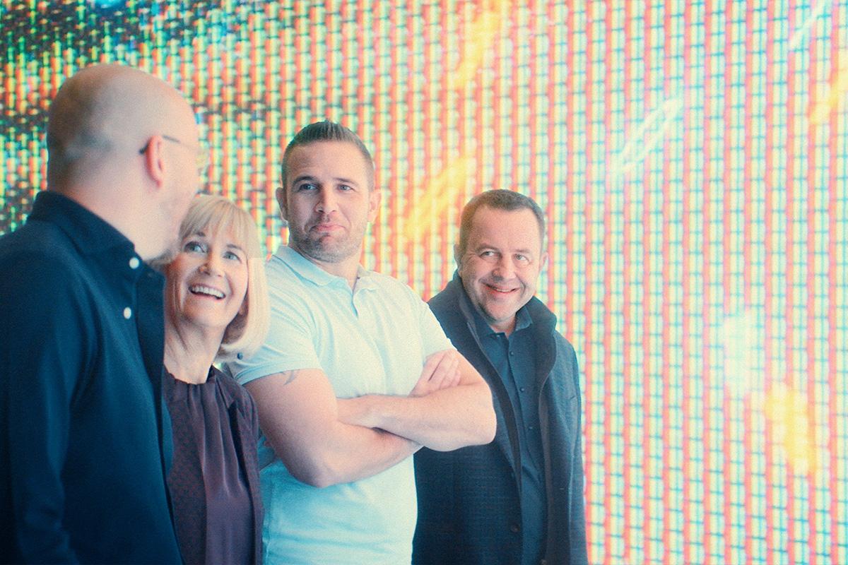 four people laughing infront of a LED screen