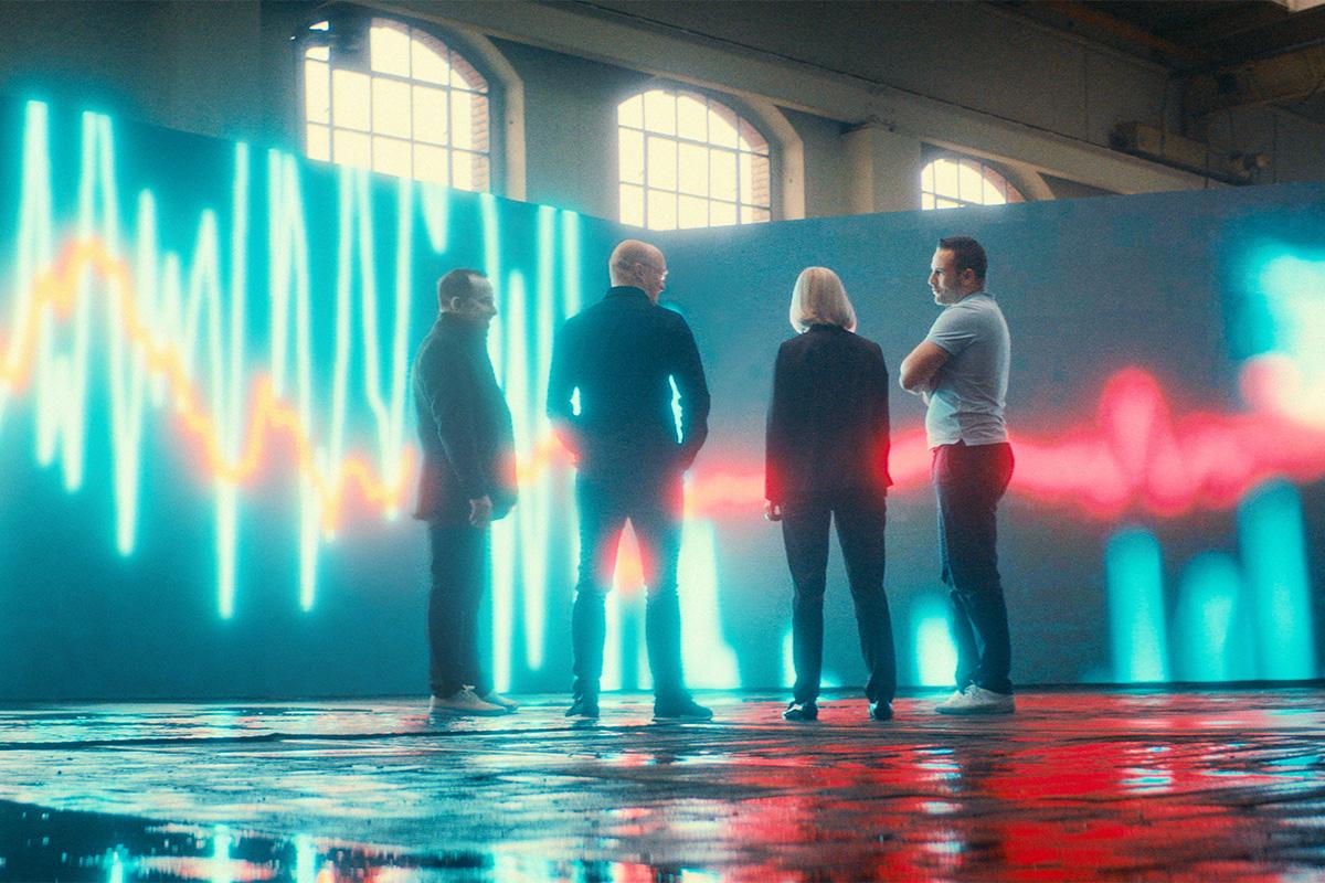 Four people discuss in font of a big LED-Screen